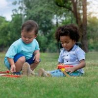 Two multiracial children sit on a lawn playing with musical instruments