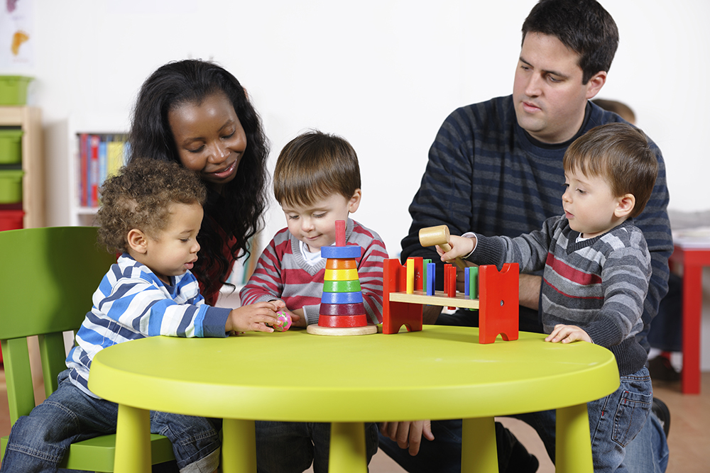 Toddlers playing with toys at a small table with parents sitting with them