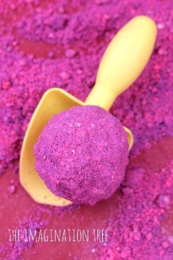 A yellow shovel holding a ball of bright pink colored sand