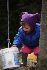 A toddler reaches into a bucket while playing outside