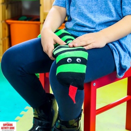 A close up of a striped sock toy with googly eyes on a kids lap