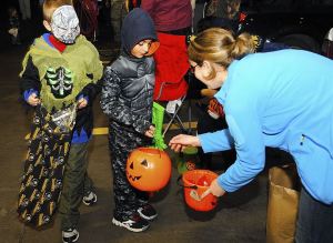 A woman drops candy into a pumpkin bucket a boy dressed up as batman for Halloween